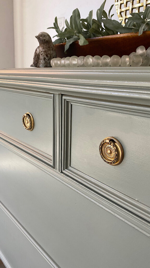 Close up photo of a hand painted dresser in light green with gold hardware.