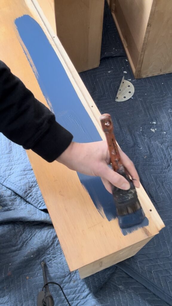 Using a paintbrush to paint navy paint on dresser drawer front.