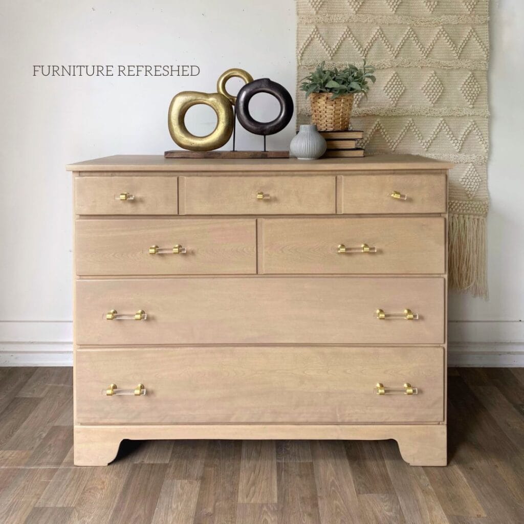 Photo of a maple 4 drawer dresser that has been bleached and paint washed. Gold and acrylic hardware. Staged with decorative accent on the top.