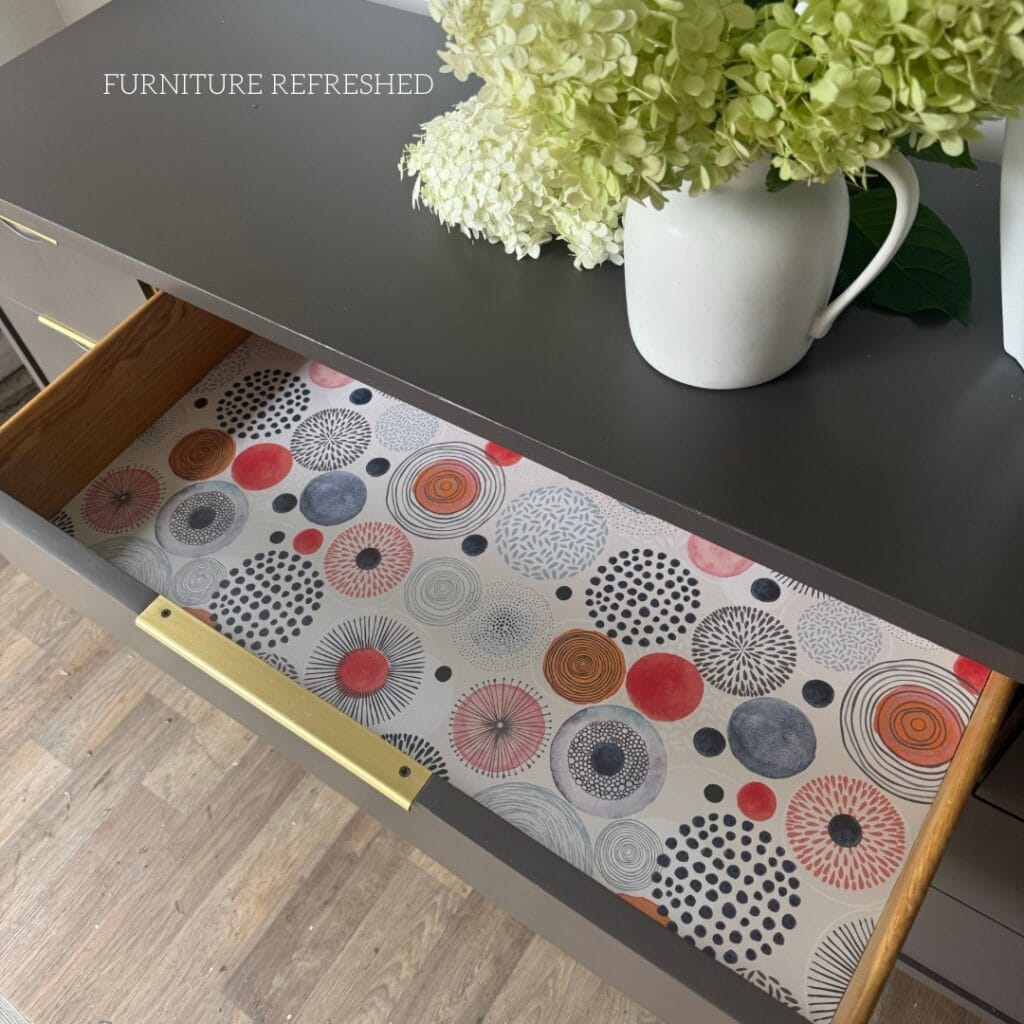 Inside the top drawer of the dresser with patterned circle and dots wallpaper as a drawer liner.