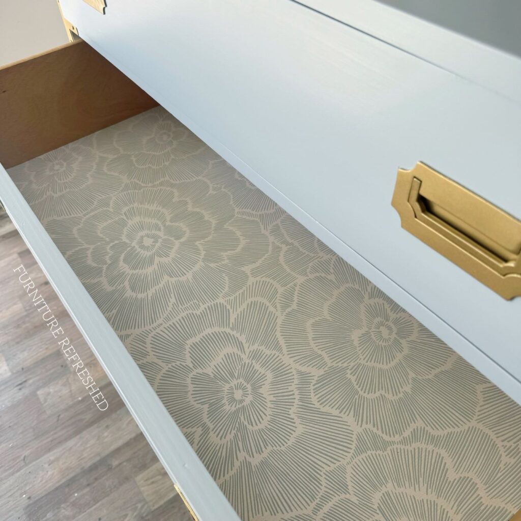 Inside of the drawer of the dresser in this makeover. Drawer is lined with blue and white floral peel and stick wallpaper.