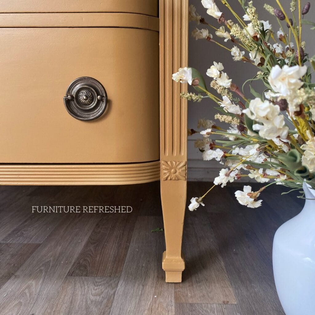 Close up view of the bottom corner of a yellow painted dresser. Shows aged vintage Hepplewhite hardware.