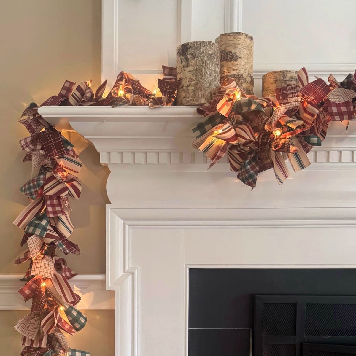 Close up of mantel with lighted Christmas fabric garland and birch bark candles.