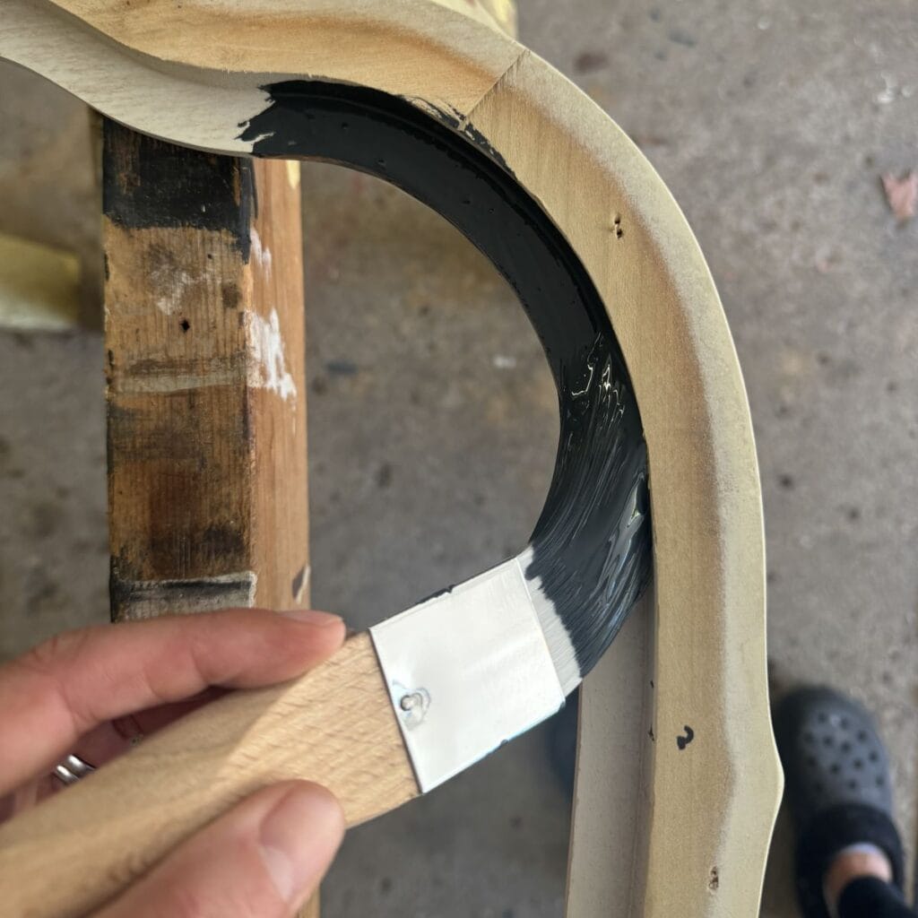 A photo of my hand painting the back of a mirror frame black.