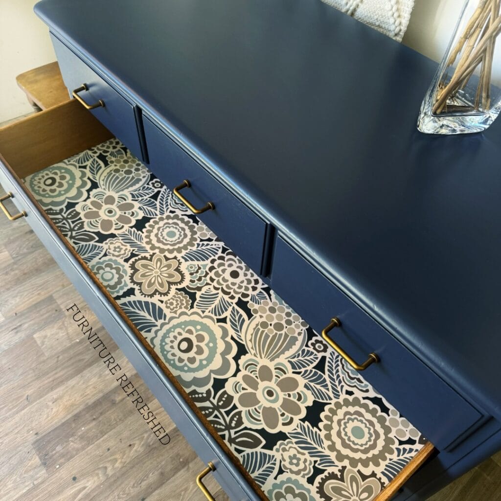 C.lose up of open dresser drawer with gray and navy floral wallpaper as a drawer liner.