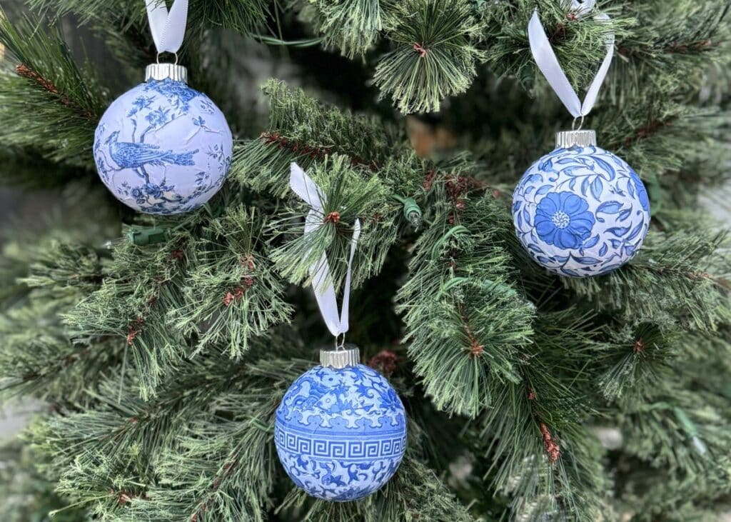 Photo of 3 Chinioserie style round Christmas ormaments with white ribbons hanging on a tree.