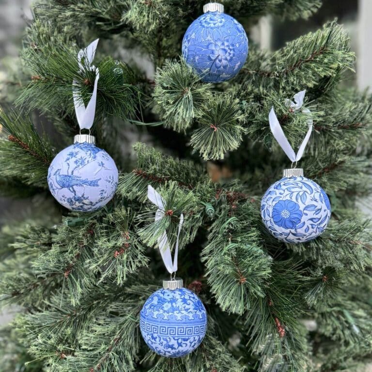 Photo of 4 Chinioserie style round Christmas ormaments with white ribbons hanging on a tree.