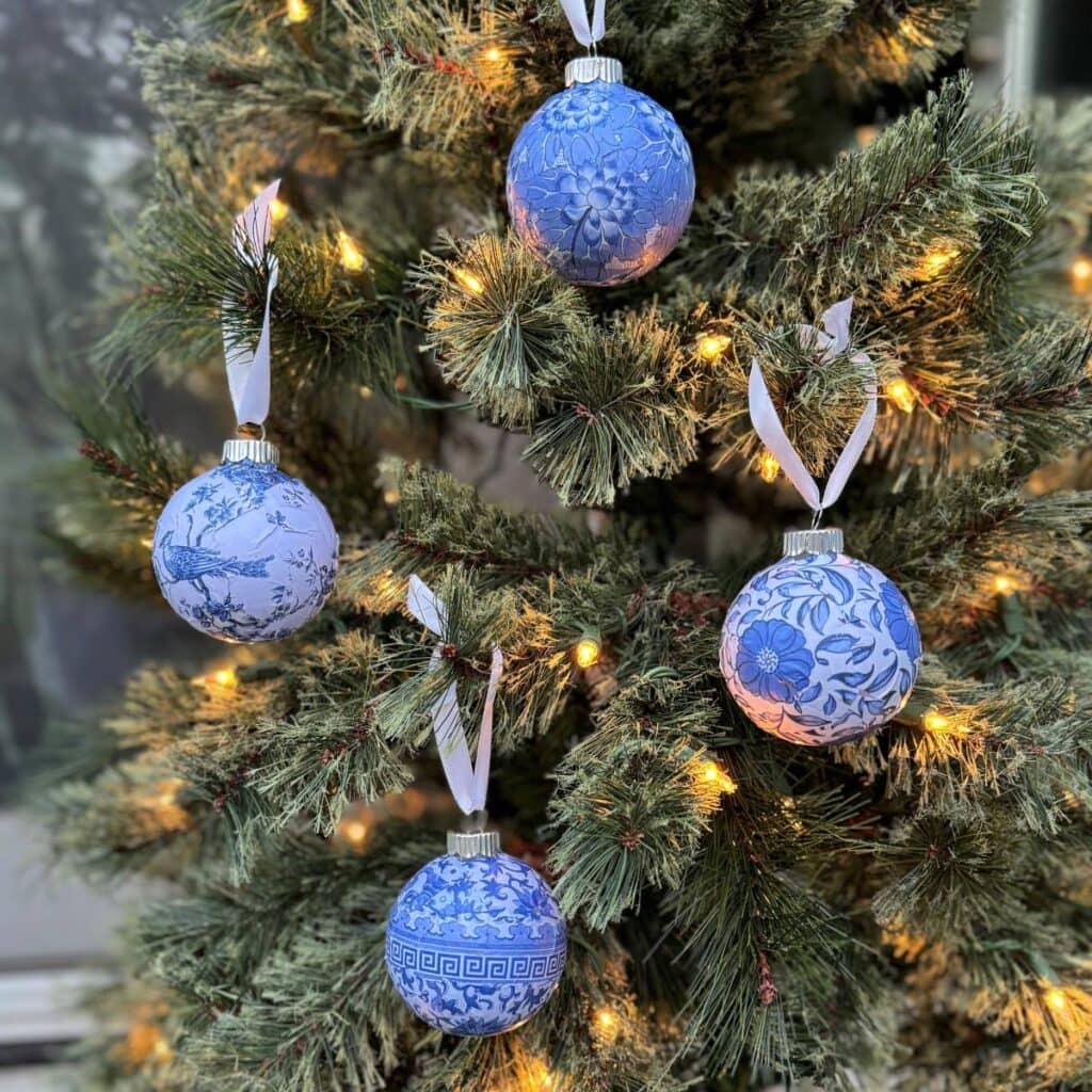 Photo of 4 Chinioserie style round Christmas ormaments with white ribbons hanging on lighted tree