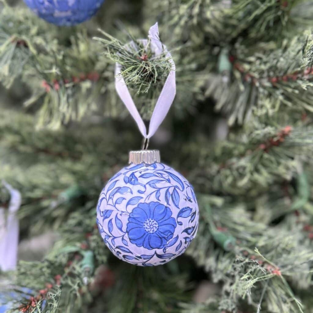 Single Chinoiserie Christmas ornament with a white ribbon hanging on a tree.