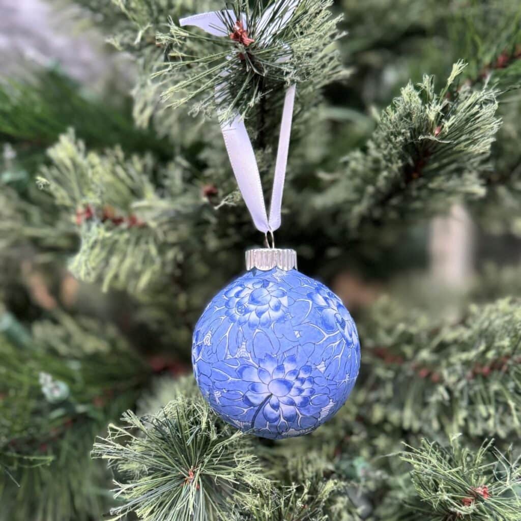 Single Chinoiserie Christmas ornament with a white ribbon hanging on a tree.