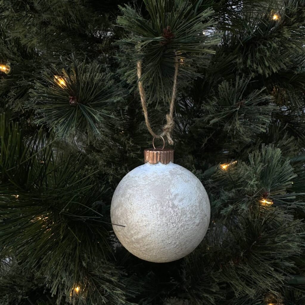 Close up of textured Christmas ornament hanging in a lighted evergreen tree.