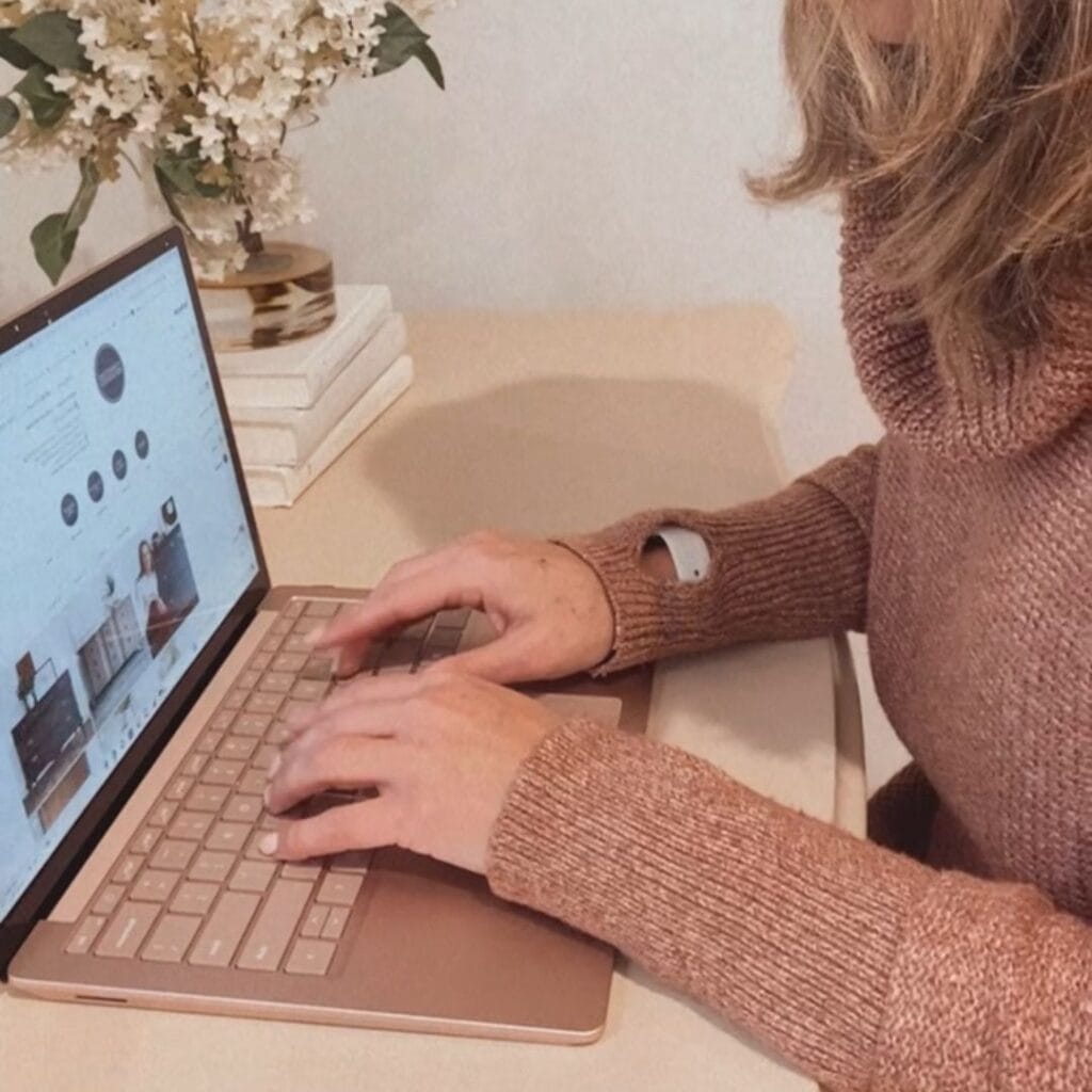 Photo of woman with a brown sweater sitting and typing on a laptop.