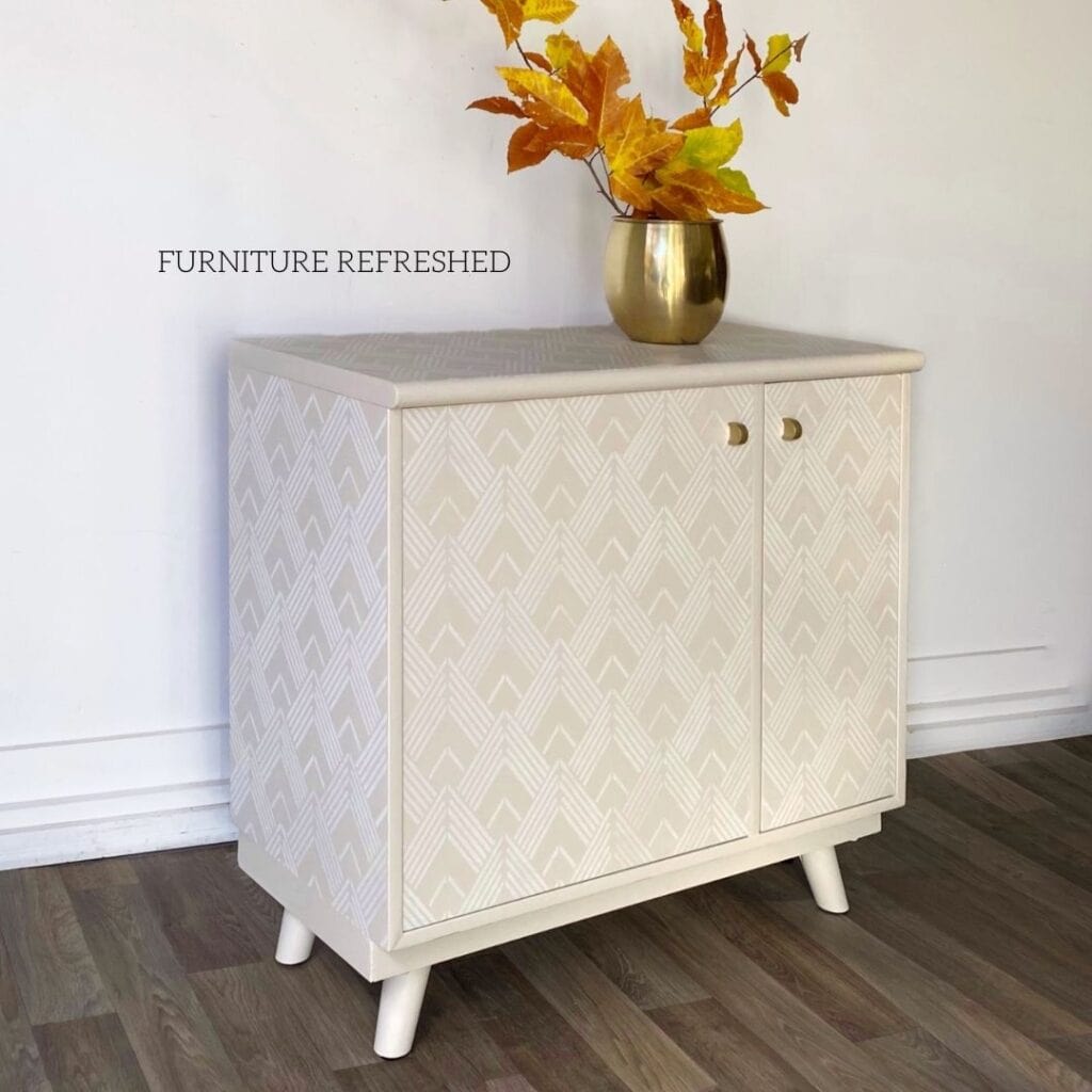 Picture of a small credenza painted in a light taupe with a white stencil pattern on top.