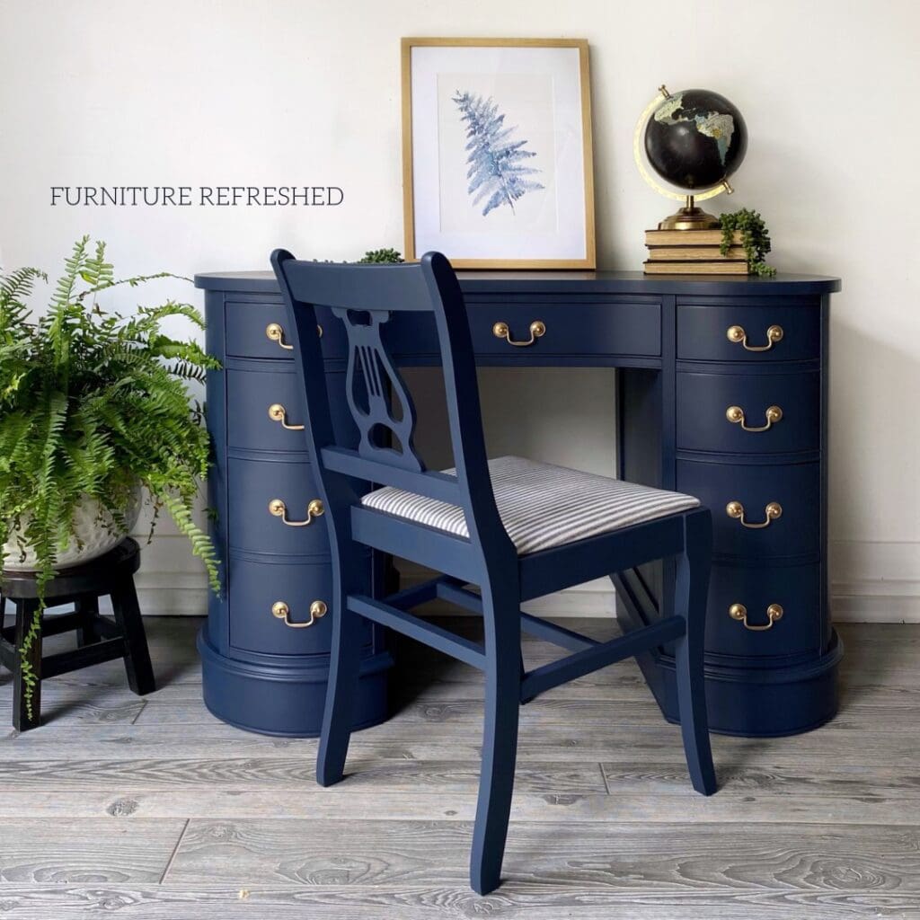 Photo of navy desk and chair, with staged decor on top and a fern to the side.