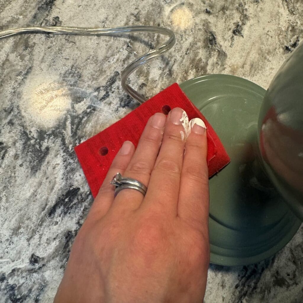 Close up photo of a hand scuff sanding the existing finish on the lamp.